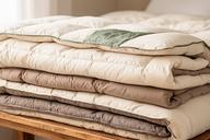 Layered natural and synthetic duvets folded on a wooden bedroom bench